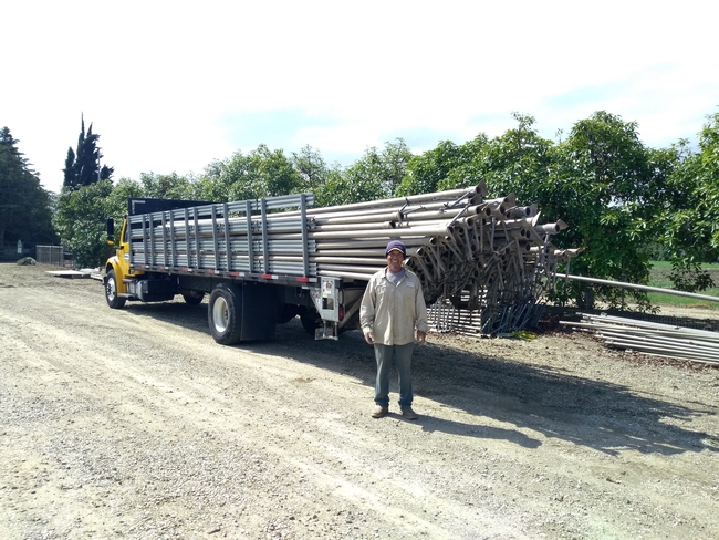 Santos stands beside a long flatbed truck loaded with irrigation pipes.