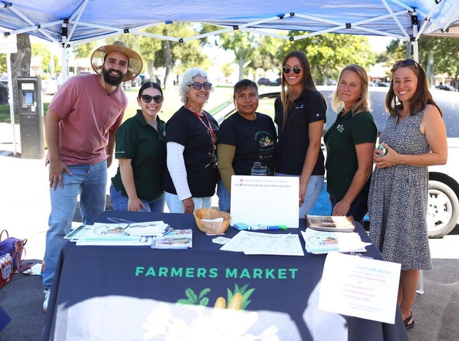 Seven people pose at a farmers market table