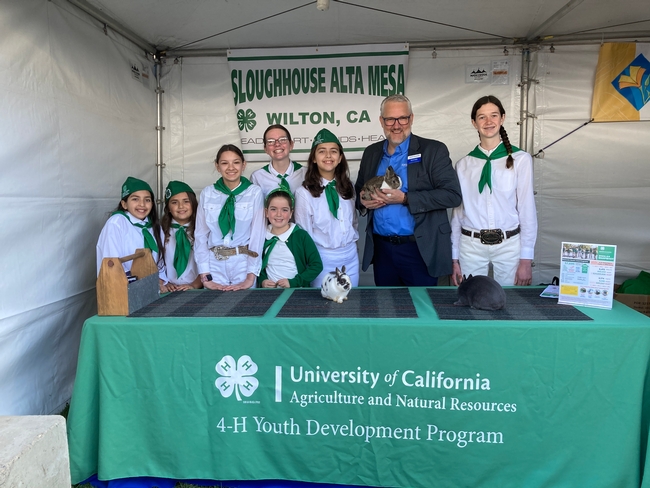 Brent Hales holds a rabbit while posing with the 4-Hers from Sloughhouse Alta Mesa from Wilton. The 4-Hers are wearing their white and green uniforms.