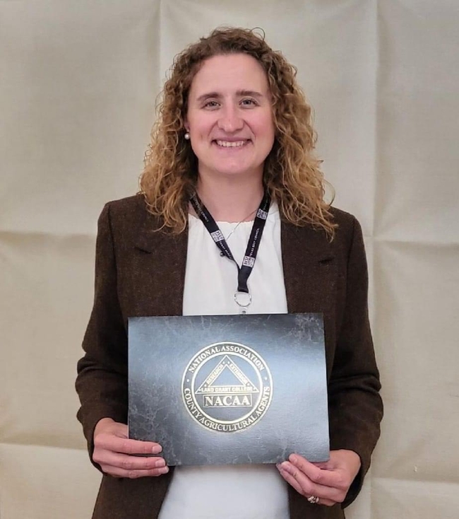 Laura Snell holds a plaque with the logo of the National Association of County Agricultural Agents.