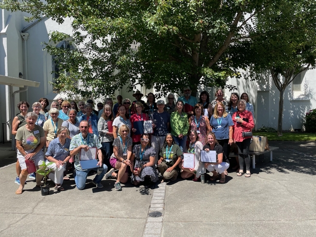 A group of 40 people pose under a tree, most holding certificates.