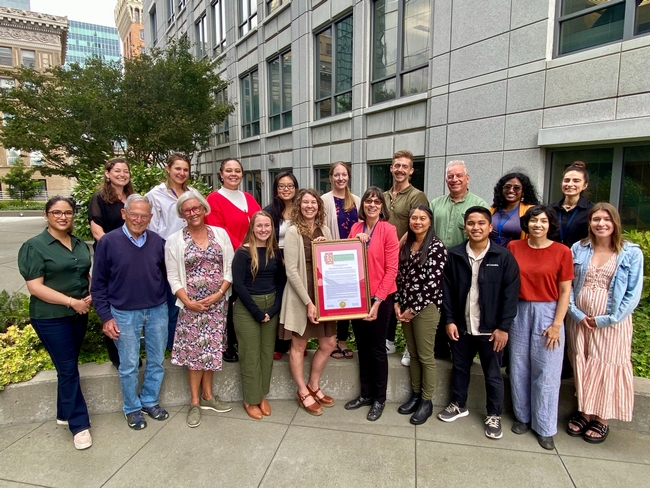 Nineteen members of the Nutrition Policy Institute flank the framed resolution in the roof garden of UC Office of the President in Oakland.