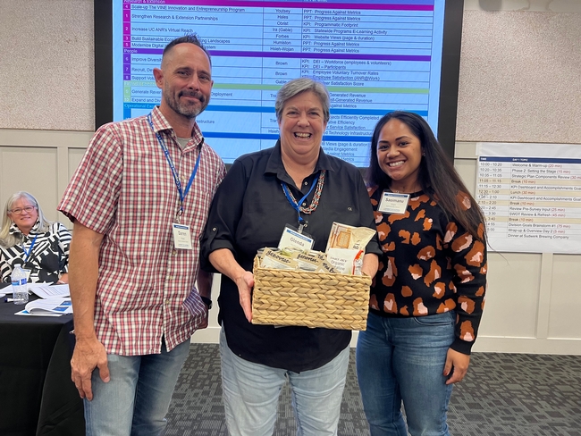 Darren Haver (left), REC System Director, and Saoimanu Sope (right), Digital Communications Specialist, present the gift of pesto to Vice President Glenda Humiston (center) from the South Coast REC Pesto Task Force.