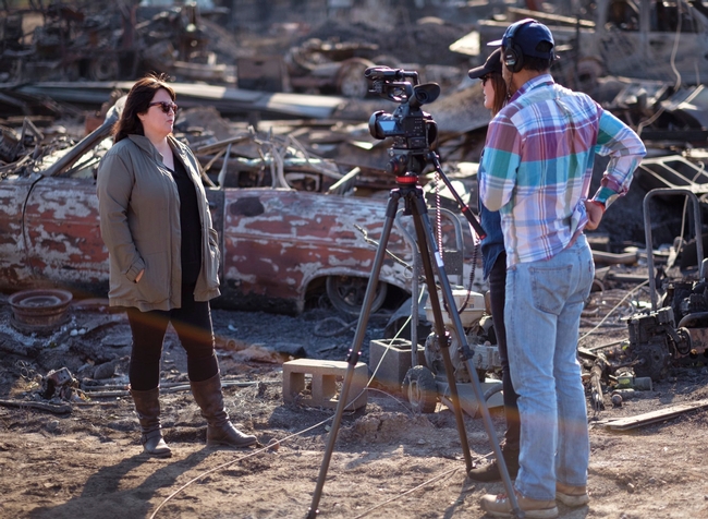 Faith Kearns stands with two film crew members beside the remains of a burned car during the Kincade Fire.
