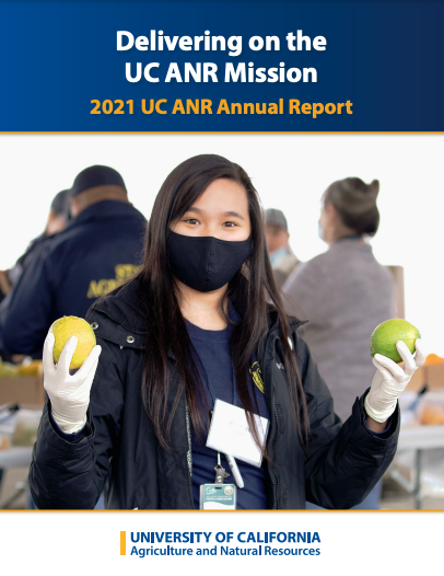 A young woman wearing a facemask holds a piece of citrus in each hand.