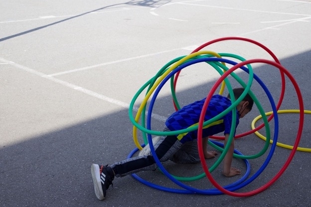 A child surrounded by red, green, blue and yellow hoops on a playground stretches his leg.