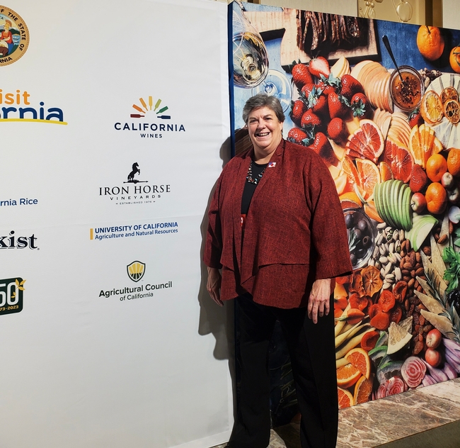 She stands beside a backdrop displaying several logos, including the UC Agriculture and Natural Resources logo.