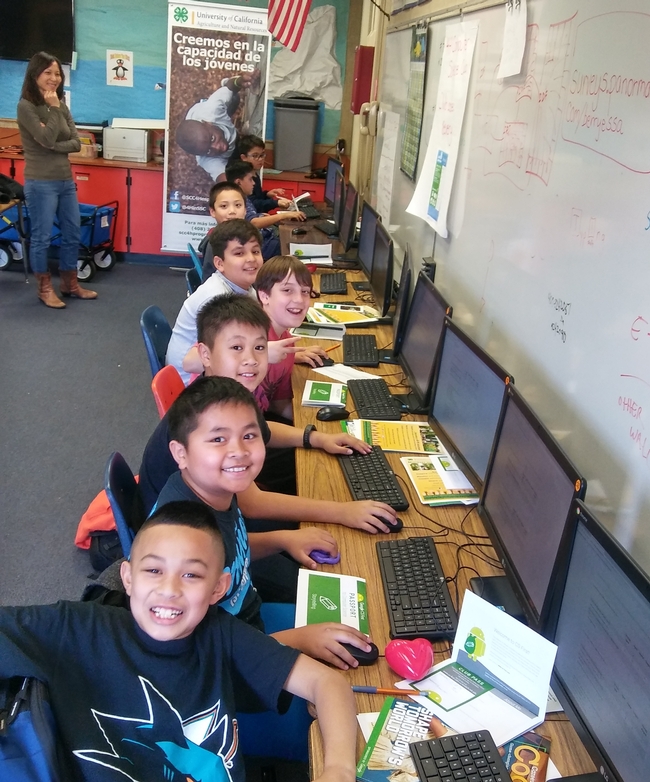 Eight smiling boys sit in a row at computers.