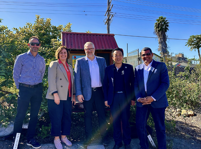 Five people standing in a garden under blue sky.