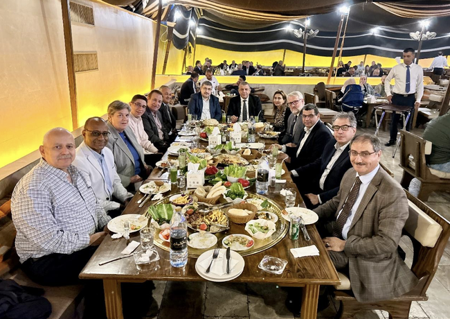 Thirteen people seated around a banquet table loaded with dishes of food.