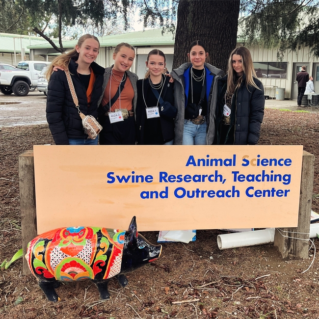 5 youth stand behind sign for Animal Science Swine Research, Teaching and Outreach Center, with a pig statue in front.