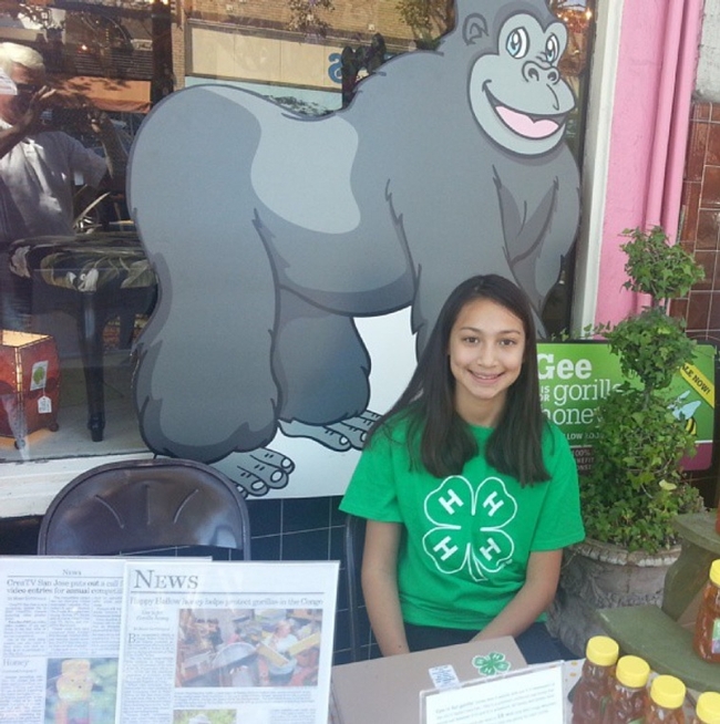 Capriana in front of a gorilla cartoon image, selling honey to help the endangered mountain gorillas in the Democratic Republic of Congo.