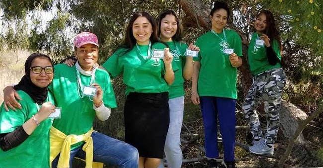 6 youth in green t-shirts pose holding their badges on lanyards