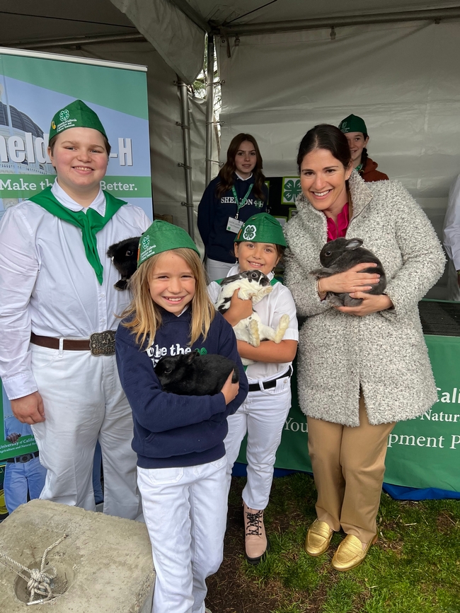 Assemblymember Rebecca Bauer-Kahan stands with three 4-H'ers. Each of them holding a rabbit.
