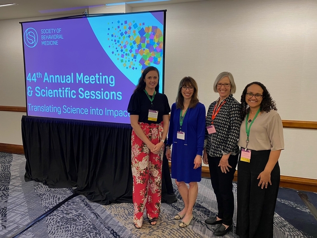 Four community health researchers stand by a screen at the Society of Behavioral Medicine Annual Meeting