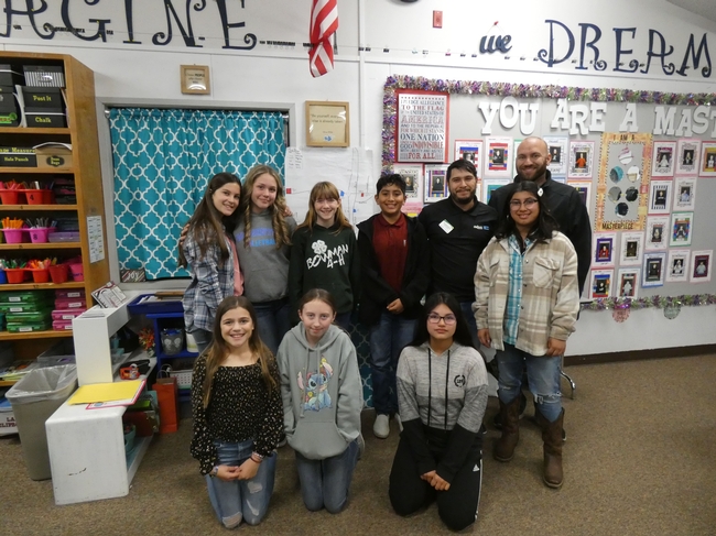 A group of sixth graders stand with educators in a classroom