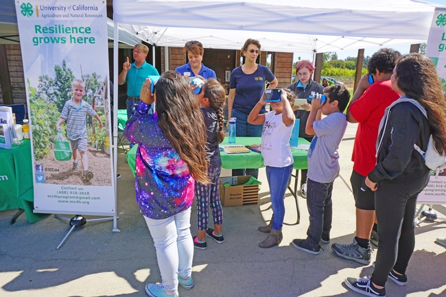 Children peer through VR goggles to see an undersea world, a 4-H activity shared with potential new members at the harvest festival. Behind the table from left are 4-H volunteer Stan Alger, 4-H program representative Sue Weaver, 4-H youth development advisor Fe Moncloa, and 4-H teen ambassador Alexa Russo.
