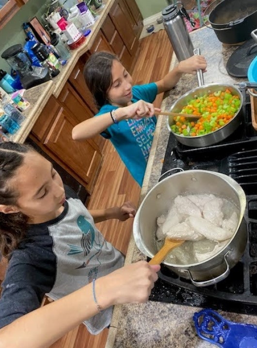 2 youth at stove stirring ingredients in 2 pots