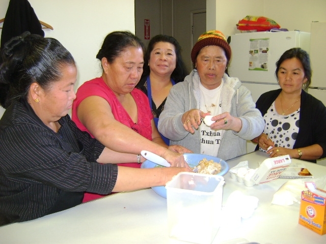 Sua, center, observes as four Hmong ladies mix food in a light blue bowl.