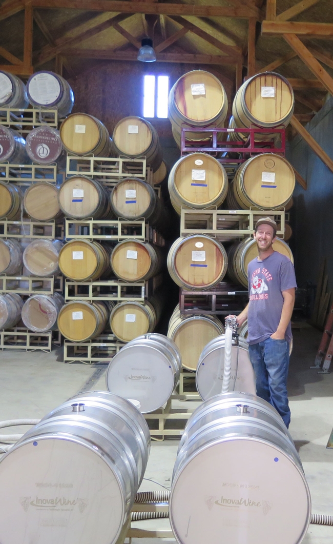 A man with a hose and barrels in a winery.