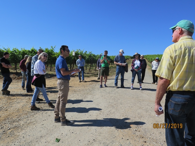 A man talking to a group of people in a vineyard.