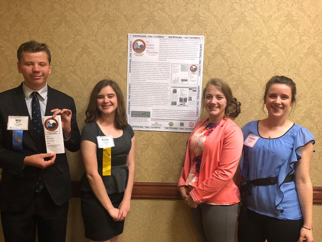 A group of four teens stand by their conference poster about their pet emergency preparedness brochure project