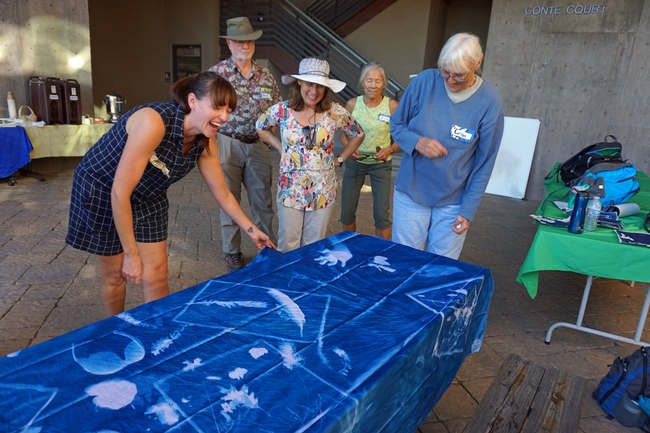 Artist Jessica Layton, left, shows a cyanotype mural project made by the group. The fabric was commercially treated with the cyanotype solutions and captured the silhouettes of a wide variety of objects, including hands, sunglasses and a water bottle.