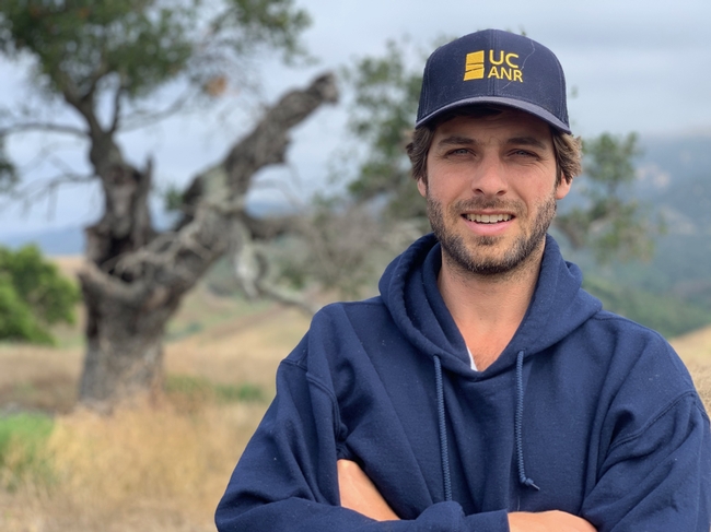 Matthew Shapero, wearing a navy blue hoodie and ANR logo hat, stands with arms folded across his chest while standing in a pastural setting.