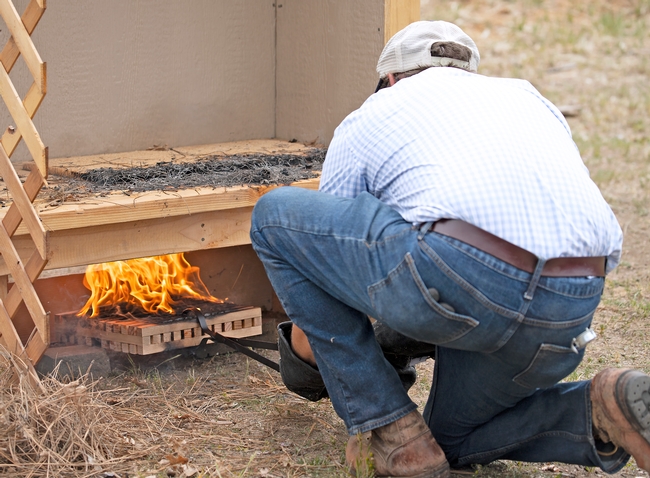 Ryan Tompkins, shown from behind, slides a flaming wooden block under a wood deck.
