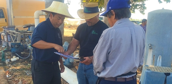 Yang points to diagram on clipboard held by a man standing between him and the farmer.