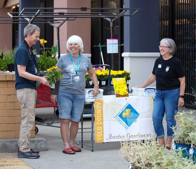 People talking in front of a UC Master Gardener Table at a garden store