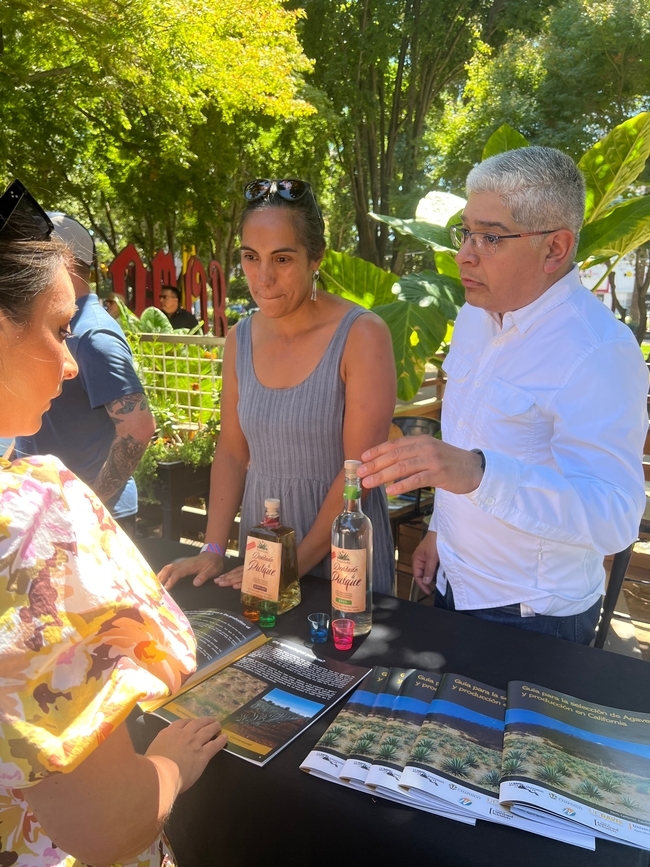 Paulina Rojas, PhD student in the UC Davis Ecology Graduate Group and research project leader Samuel Sandoval Solis, UC Cooperative Expension specialist in water resources managment offering pulque tasting to an event attendee.