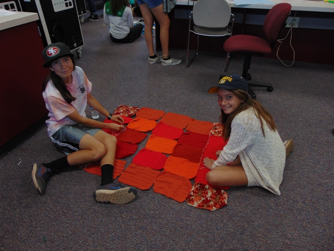 Two 4-H girls work together to piece their chosen knitted squares together using a whip stitch.