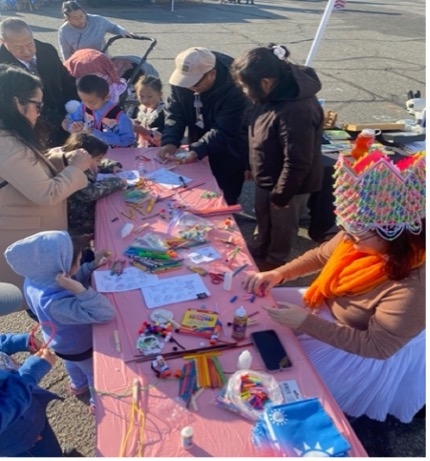 Many people sit or stand around a table with crafts.