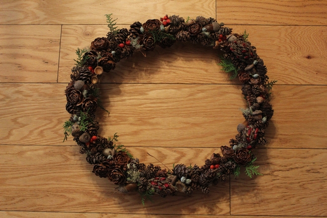 Wreath made of grapevine covered in pine cones, acorns, berries, with ribbon.