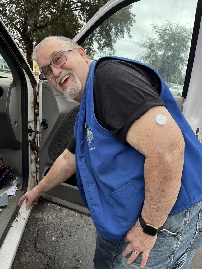 Smiling man wearing blue vest points towards an aggregate of ladybugs on the inside of his truck.
