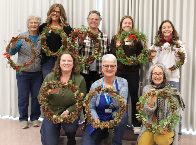 Smiling women in a group holding wreaths they made.