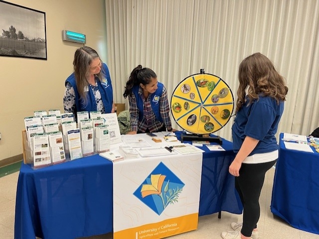 Two Master Gardeners smiling as someone spins a prize wheel.