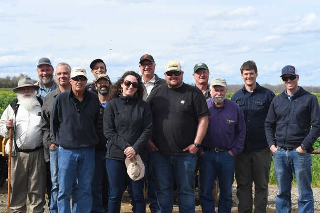 Group of farmers and Cooperative Extension academics standing in a farm, smiling for the camera.