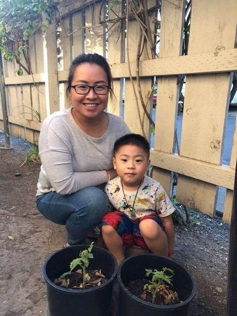 A parent and child smile next to their tomato plant