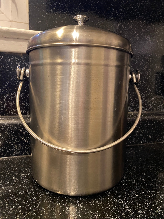 A silver, stainless steel pail with a handle and lid sitting on a kitchen counter.