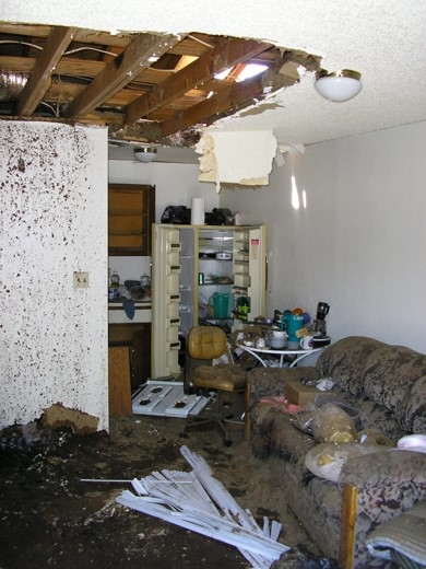 Living space with damage to ceiling and debris resulting from explosion.