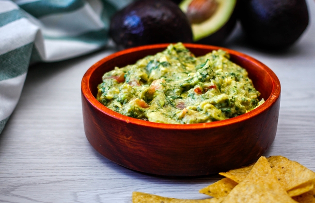Bowl of guacamole with tortilla chips on the side.