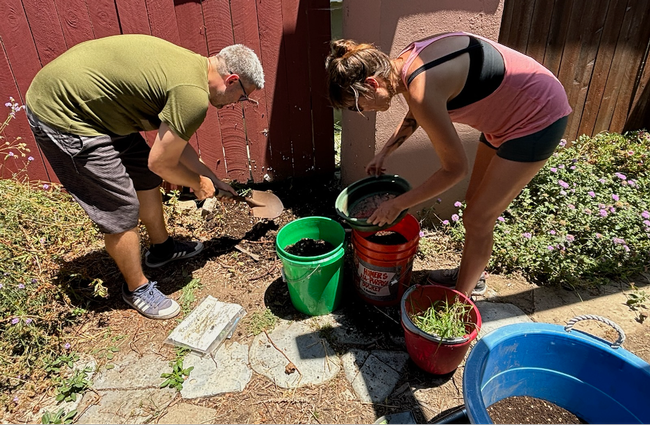 Two individuals sort finished compost into buckets.