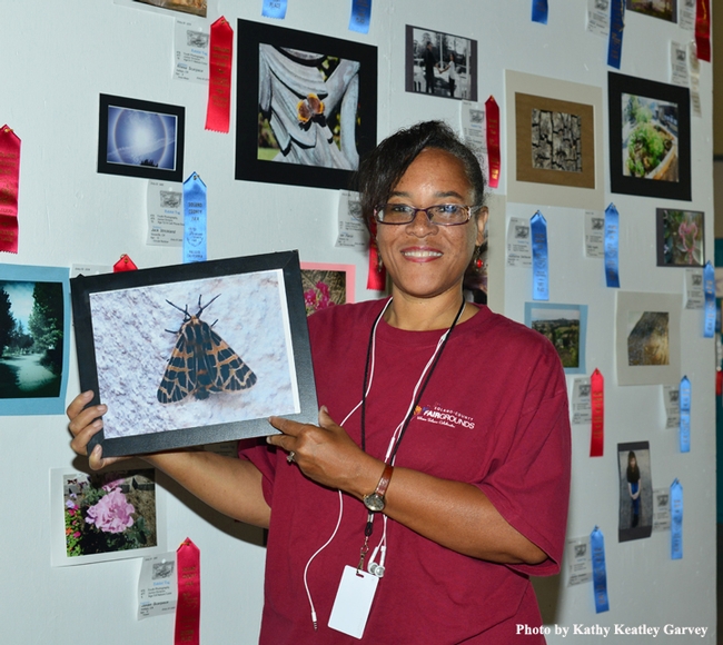 McCormack Hall assistant Iris Mayhew holds a photo of a moth, the work of 9-year-old Maximillian Burgess-Shannon of Benicia. (Photo by Kathy Keatley Garvey)