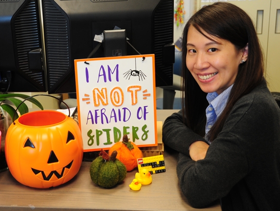 Louisa Lo, executive administrative assistant for Bruce Hammock, distinguished professor of entomology, sits next a sign proclaiming she is not afraid of spiders. She is. (Photo by Kathy Keatley Garvey)