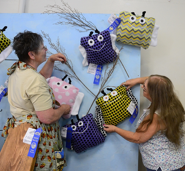 Dixon May Fair Youth Building superintendent Building superintendent Stephanie Hill (left) of Yuba City and assistant building superintendent Pat Connelly of Vacaville hang bumble bee pillow, the work of Solano County 4-H'ers. (Photo by Kathy Keatley Garvey)