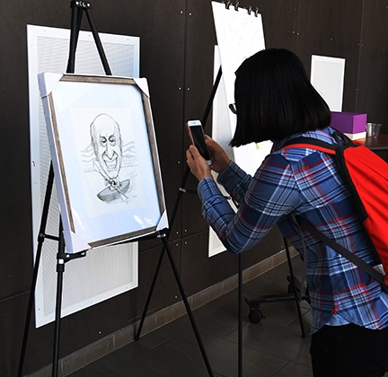 An attendee at the Hammock lab reunion photographs an illustration of him, the work of Dennis Preston of East Lansing, Mich. (Photo by Kathy Keatley Garvey)