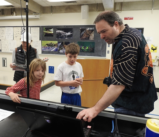 UC Davis medical entomologist Geoffrey Attardo shows Sebastian and Kamila Ehrlich examples of  what insects they might want to see in virtual reality. In back is their mother, Carollina Ehrlich. (Photo by Kathy Keatley Garvey)
