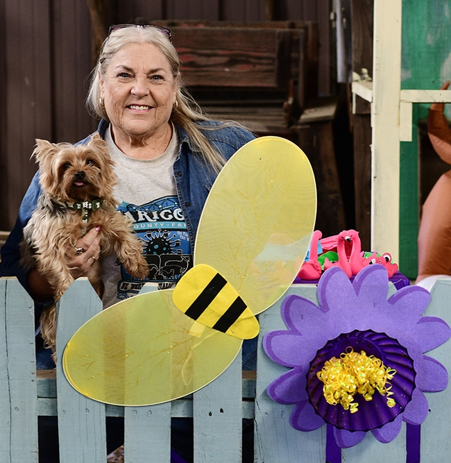 It's all the buzz! Pat Connelly, superintendent of the Dixon May Fair Floriculture Building, crafted this motif of bees and a blossom to decorate the building. With her is her 9-year-old Yorkie, Carly. (Photo by Kathy Keatley Garvey)